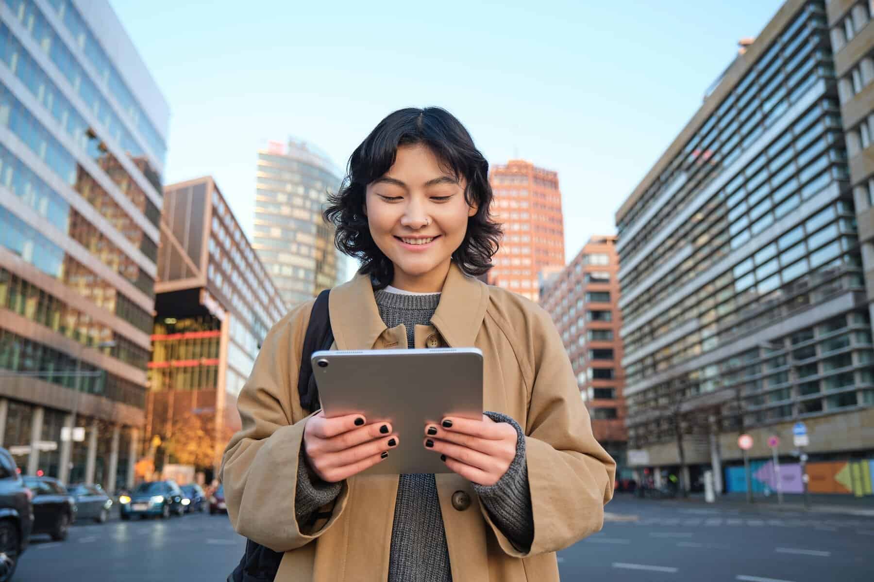 Portrait of happy korean girl smiles, walks in city with digital tablet and backpack, uses her